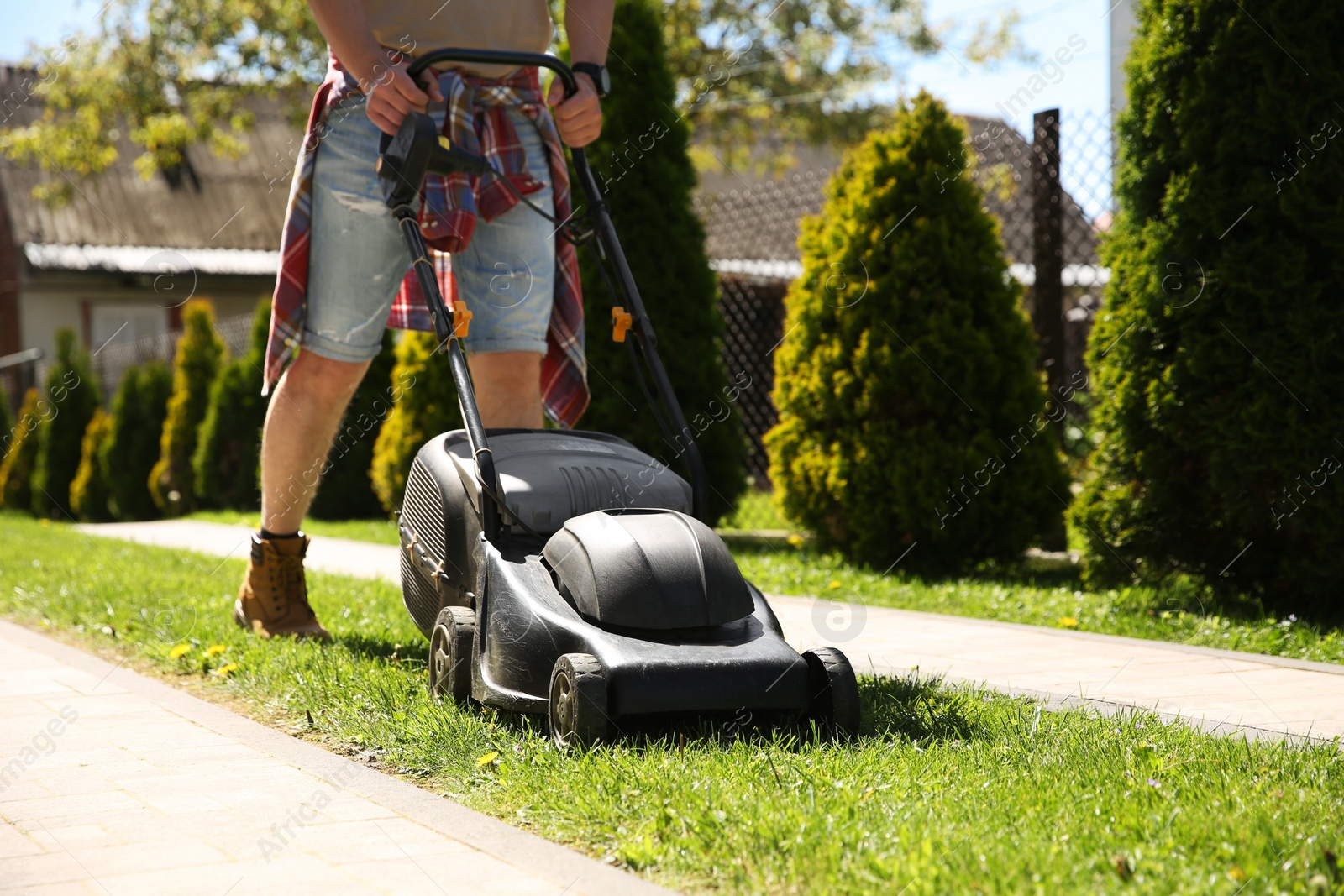 Photo of Man cutting green grass with lawn mower on backyard, closeup