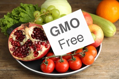 Photo of Fresh fruits, vegetables and card with text GMO Free on wooden table