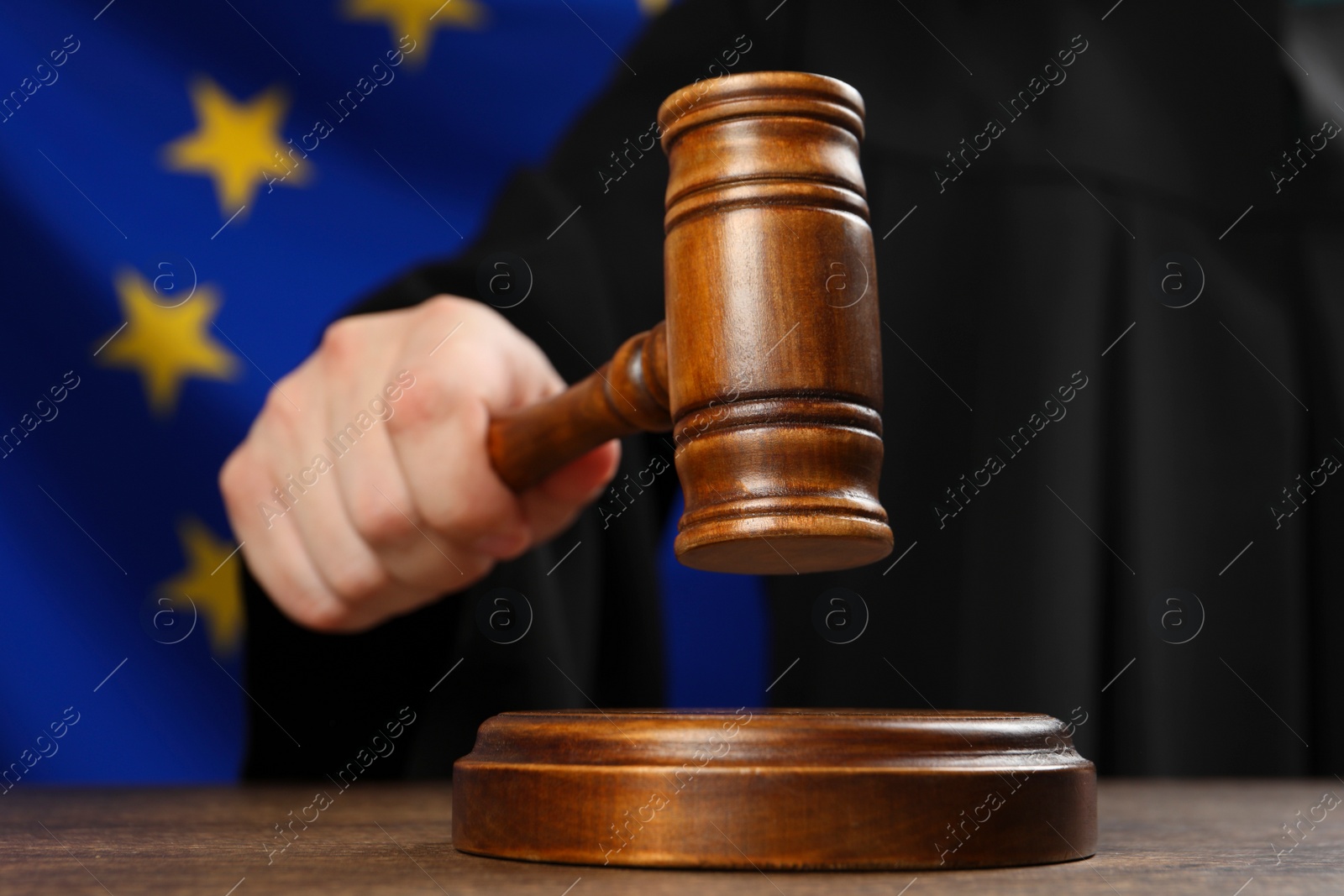 Photo of Judge with gavel at wooden table against flag of European Union, closeup