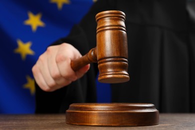 Judge with gavel at wooden table against flag of European Union, closeup