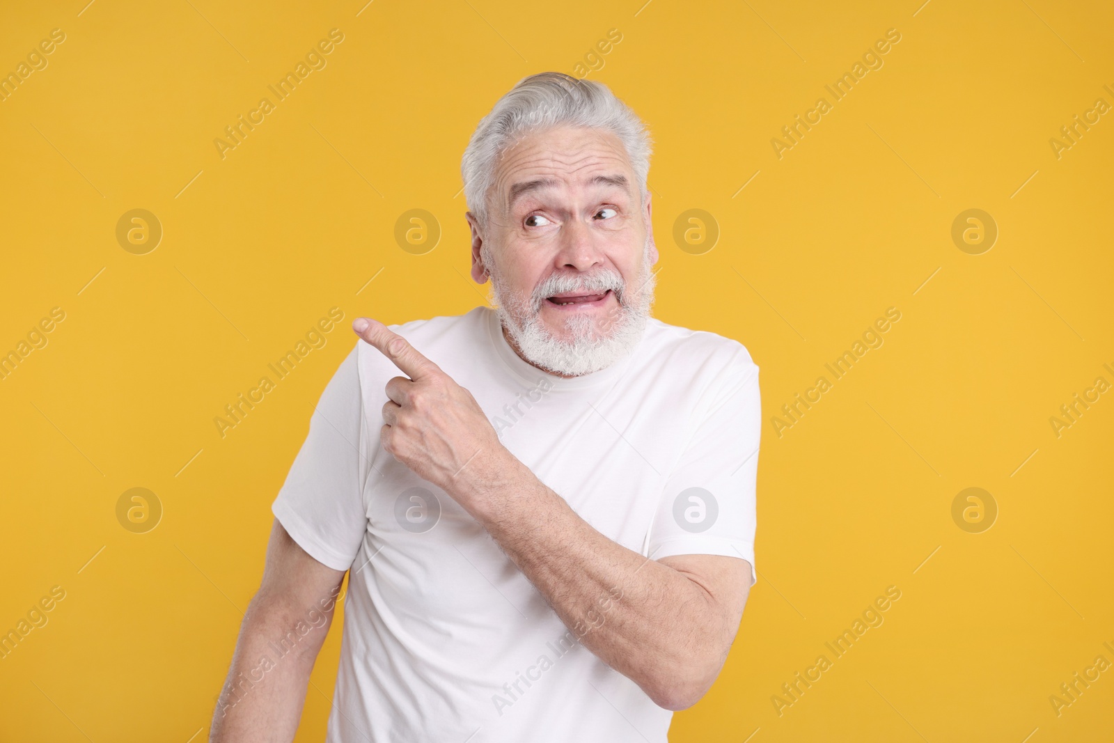 Photo of Surprised senior man pointing at something on yellow background