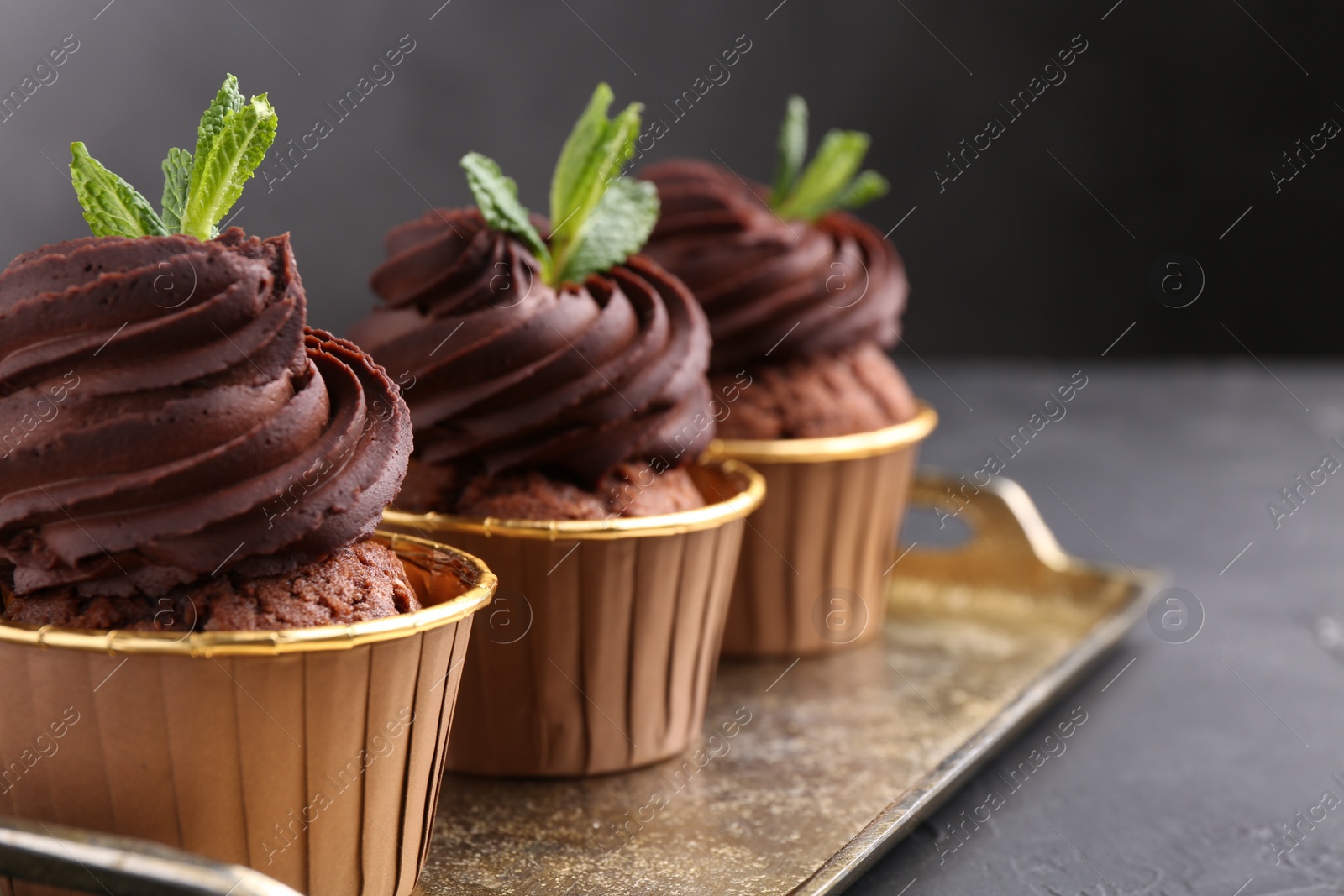 Photo of Delicious chocolate cupcakes with mint on black textured table, closeup