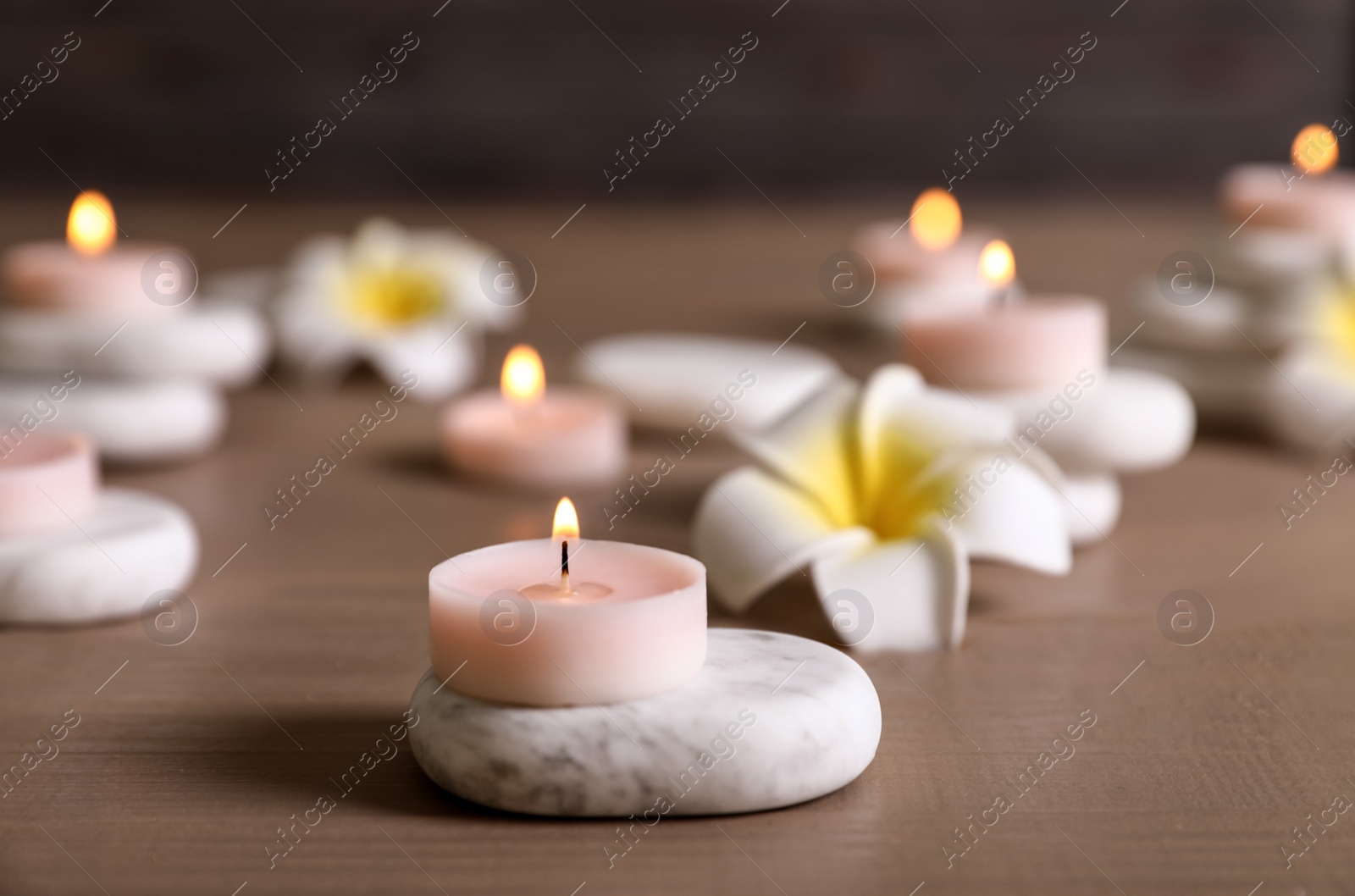 Photo of Composition of spa stones, flowers and burning candles on wooden table