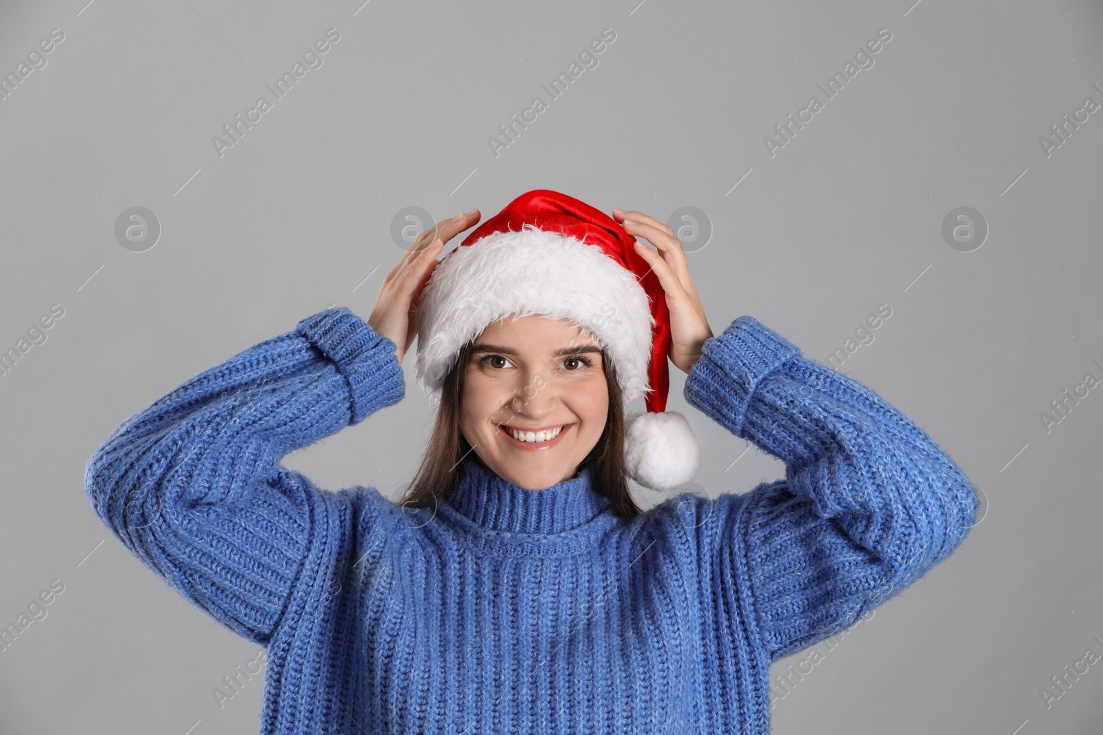 Photo of Pretty woman in Santa hat and blue sweater on grey background
