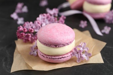 Delicious violet macaron and lilac flowers on black table, closeup