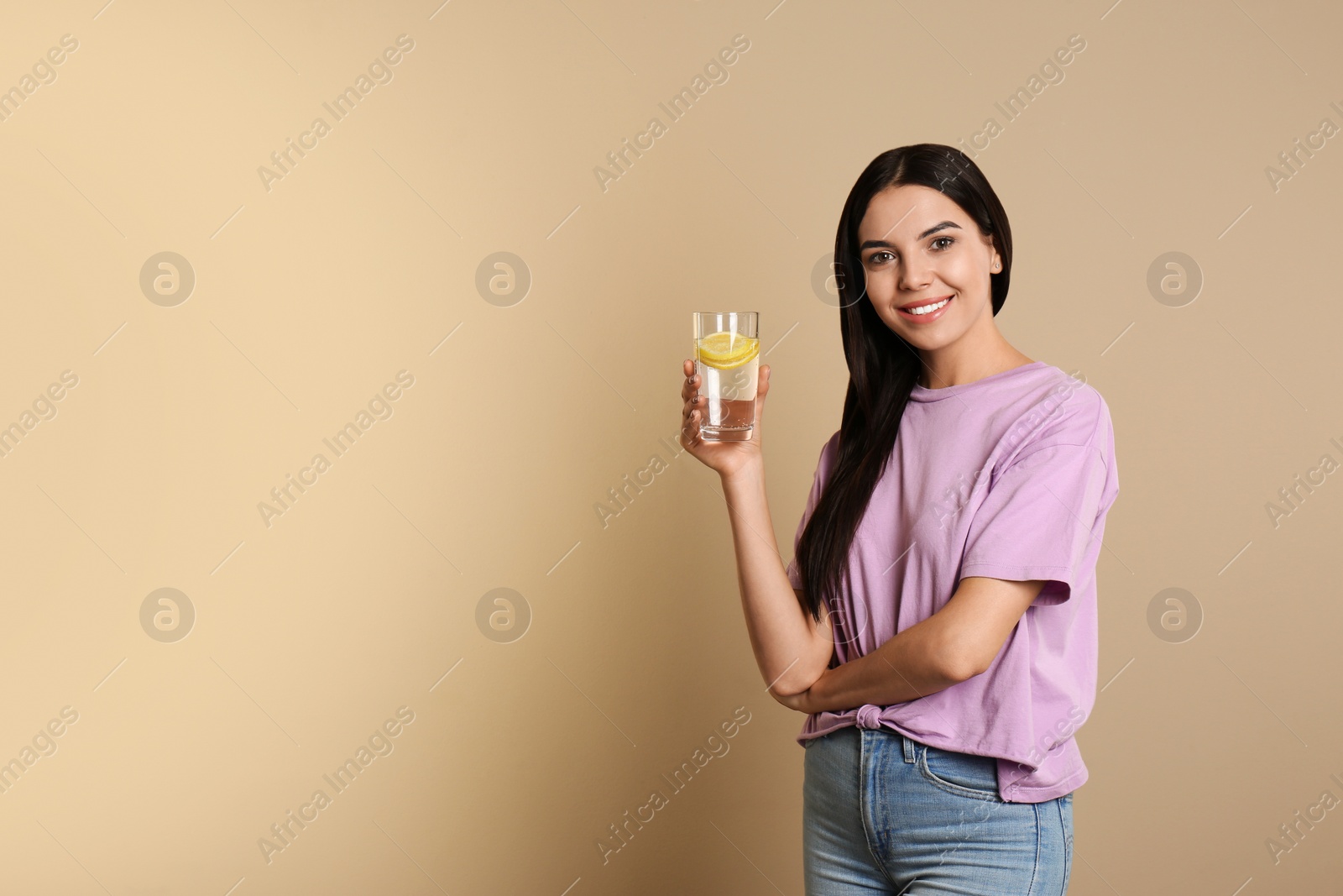 Photo of Beautiful young woman with tasty lemon water on beige background. Space for text