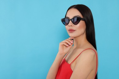 Photo of Attractive serious woman in fashionable sunglasses against light blue background. Space for text