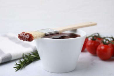Photo of Marinade in bowl and basting brush on white table, closeup