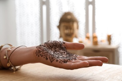 Photo of Woman with henna tattoo on palm at table indoors, closeup. Traditional mehndi ornament