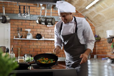 Photo of Professional chef frying fresh vegetables on stove in restaurant kitchen