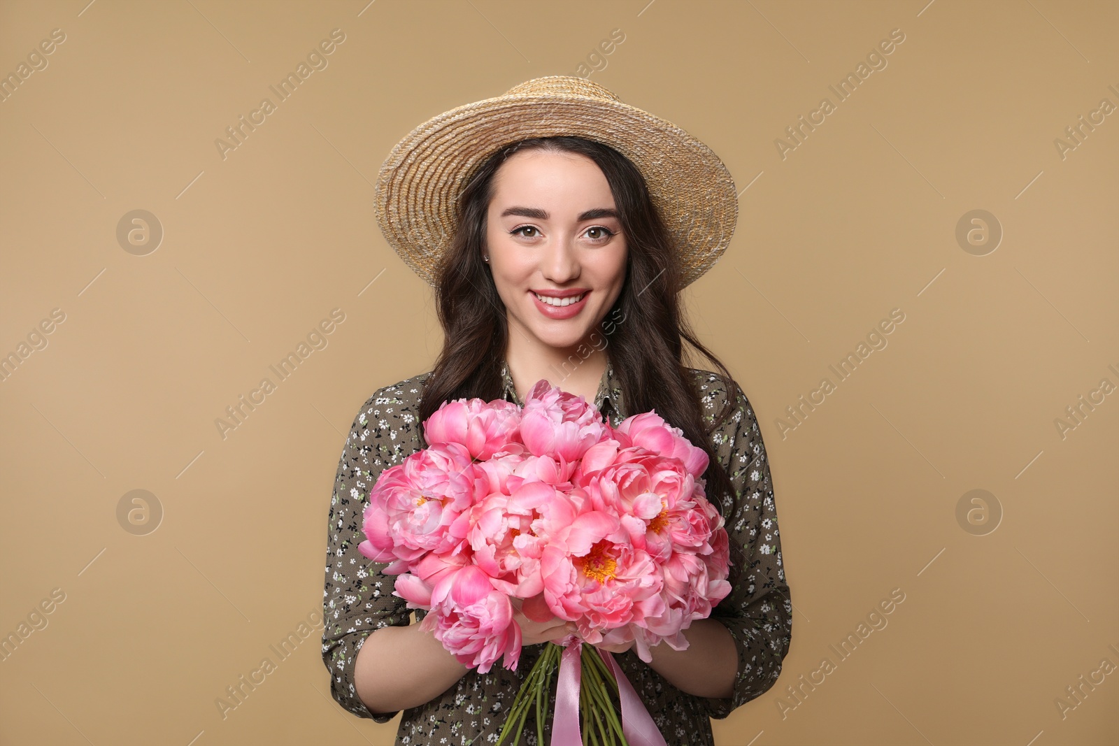 Photo of Beautiful young woman in straw hat with bouquet of pink peonies against light brown background