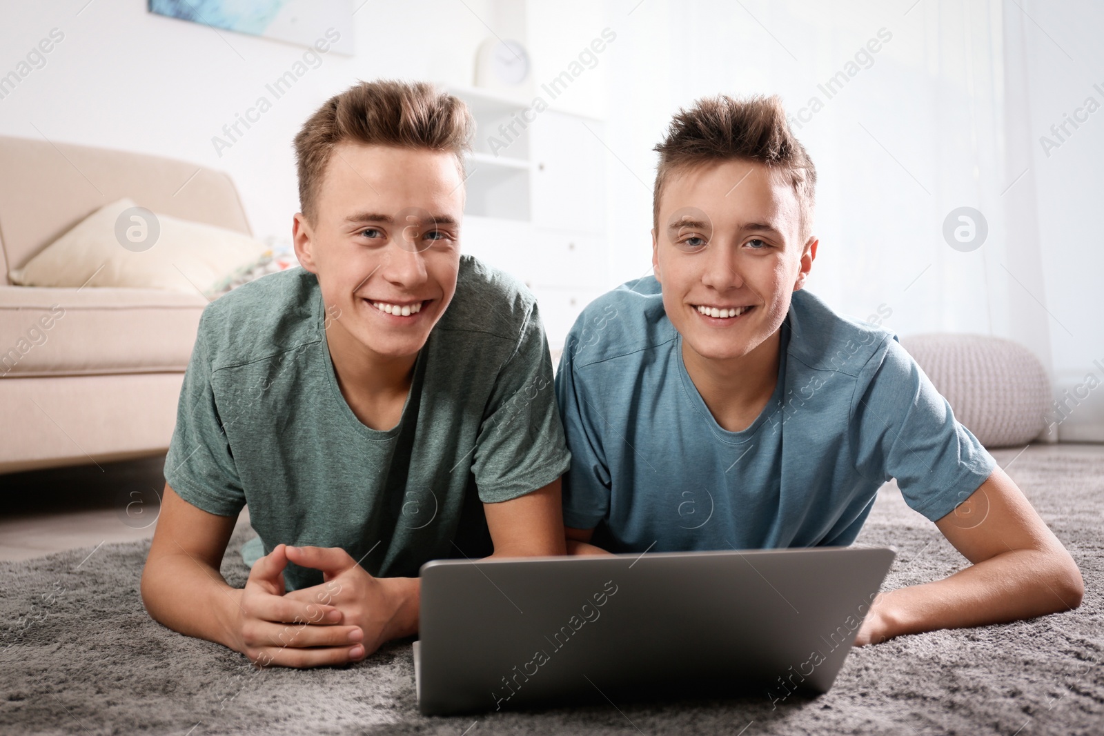 Photo of Teenage twin brothers using laptop together in living room