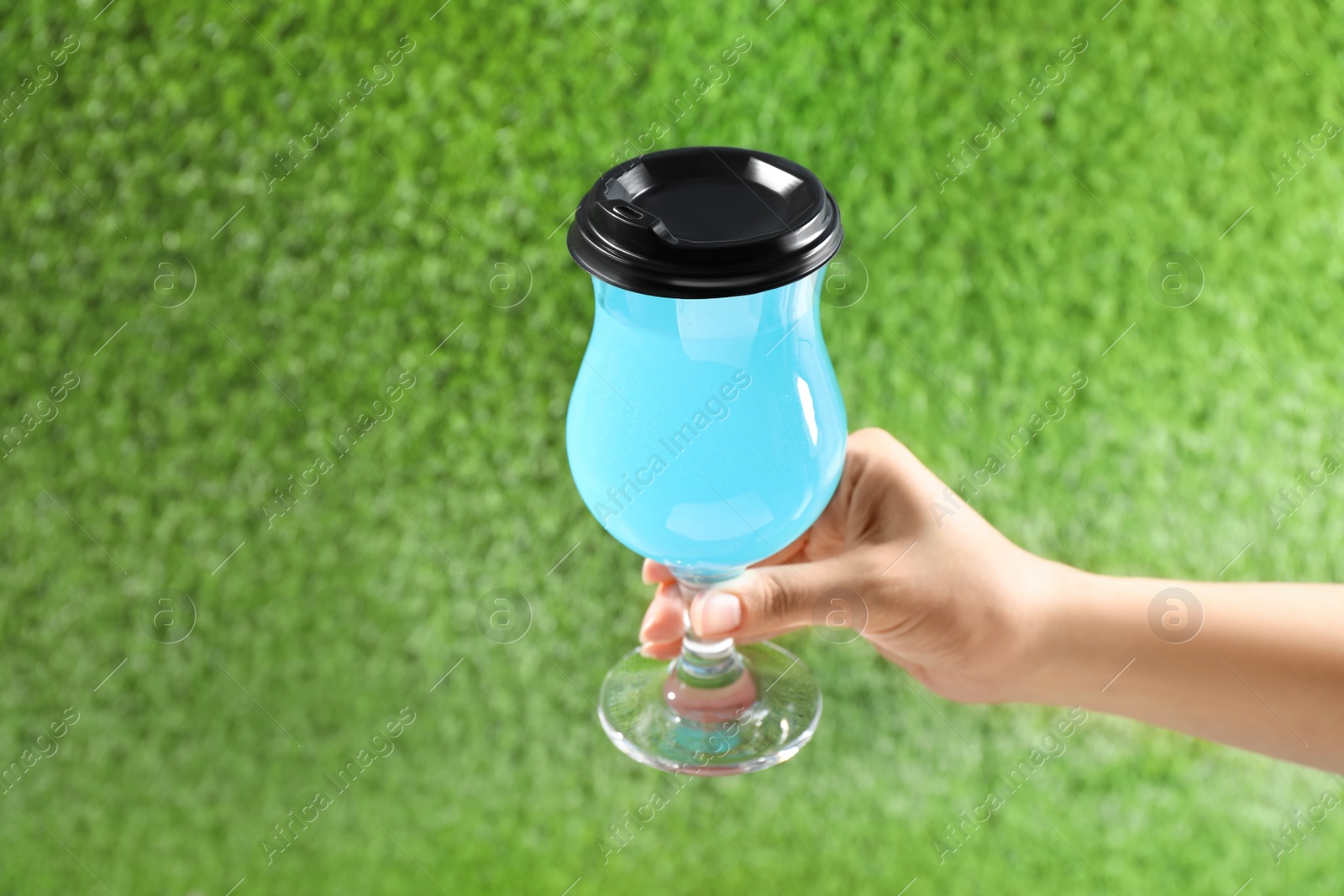 Photo of Woman holding glass of light blue drink against green grass, closeup