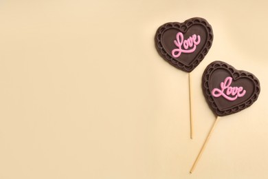 Photo of Chocolate heart shaped lollipops with word Love on beige background, flat lay. Space for text