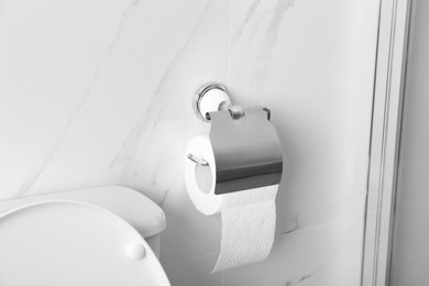 Photo of Holder with toilet paper roll on wall in bathroom
