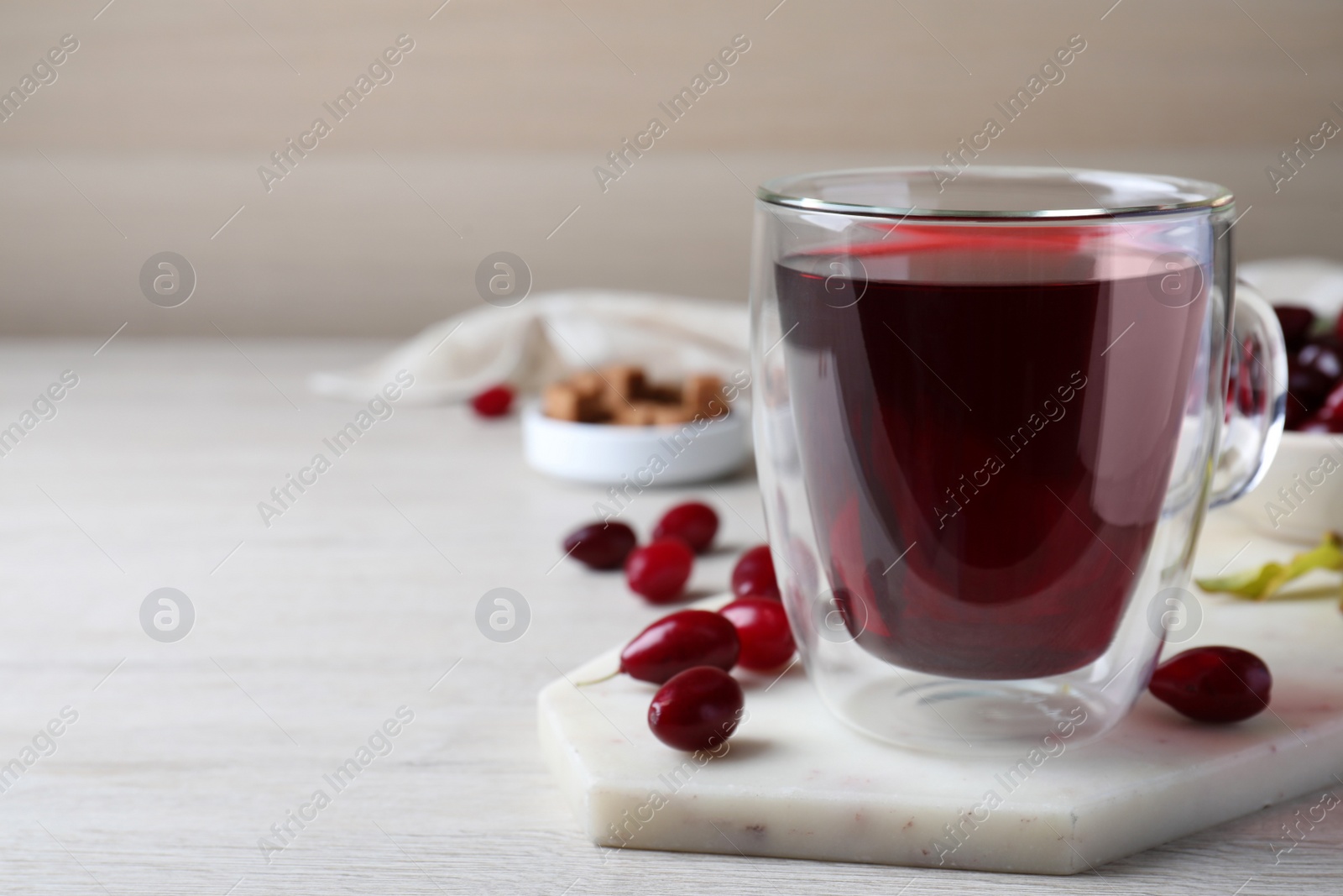 Photo of Glass cup of fresh dogwood tea and berries on white wooden table. Space for text