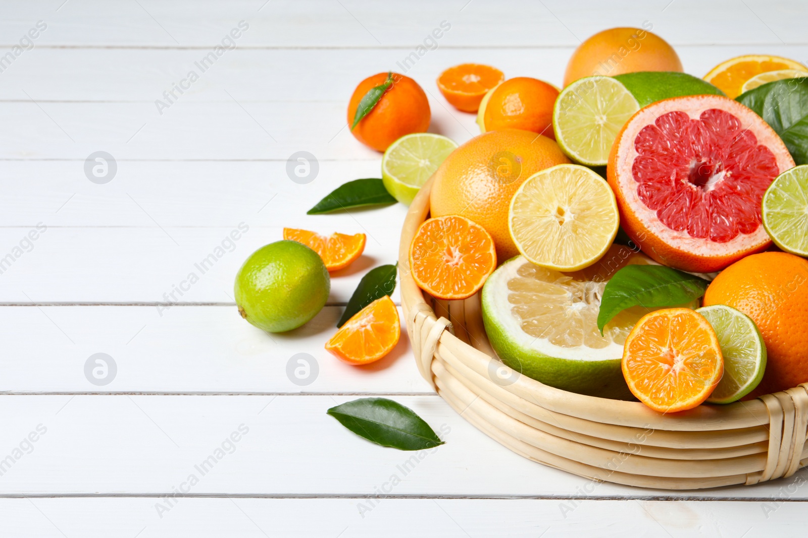 Photo of Different ripe citrus fruits with green leaves on white wooden table. Space for text
