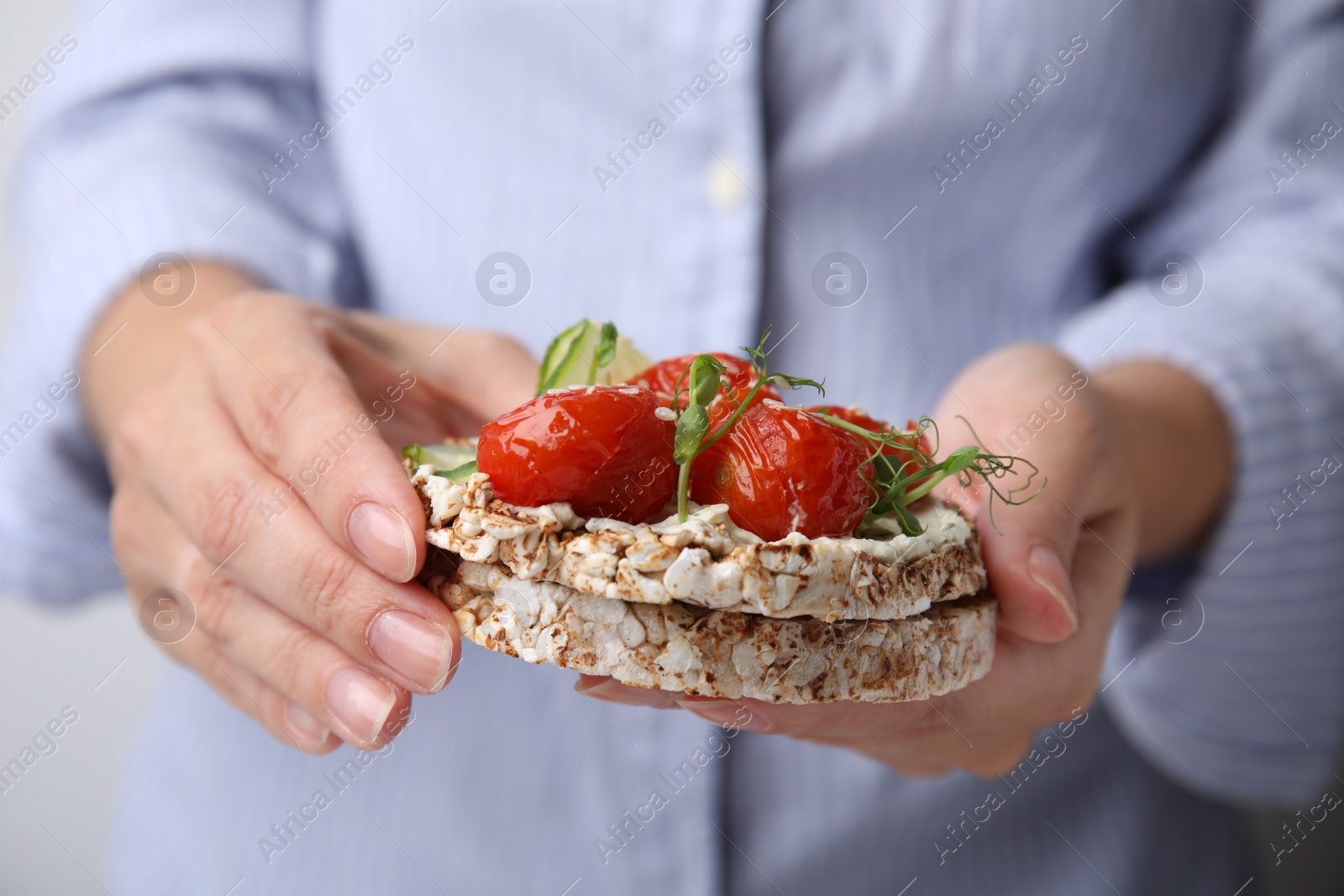 Photo of Woman holding crunchy buckwheat cakes with cream cheese, tomatoes and microgreens, closeup