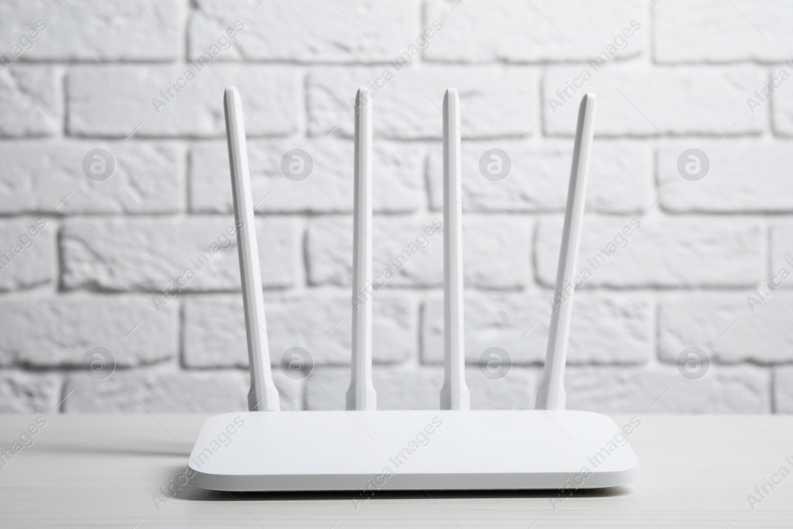 Photo of New Wi-Fi router on white wooden table against brick wall