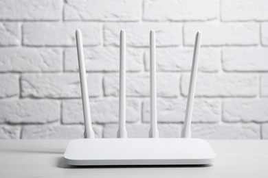 Photo of New Wi-Fi router on white wooden table against brick wall