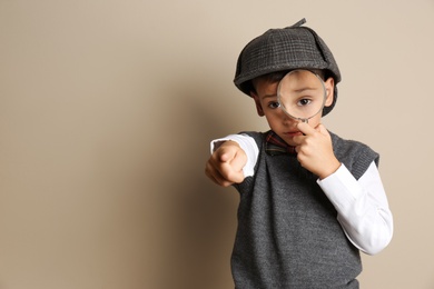 Photo of Little boy with magnifying glass playing detective on beige background. Space for text