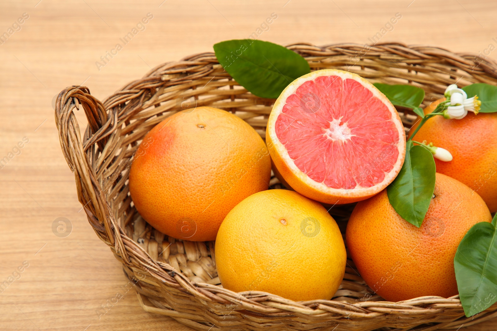 Photo of Wicker basket with fresh ripe grapefruits and green leaves on wooden table