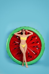 Photo of Young woman in stylish swimsuit near inflatable mattress against light blue background