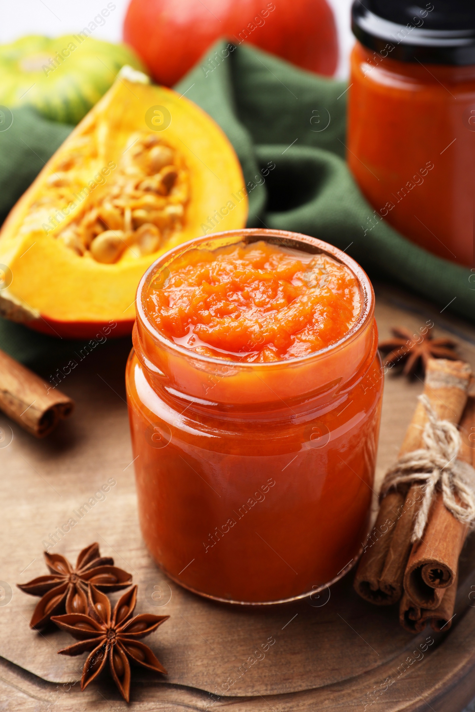 Photo of Jar of delicious pumpkin jam and ingredients on tiled surface, closeup