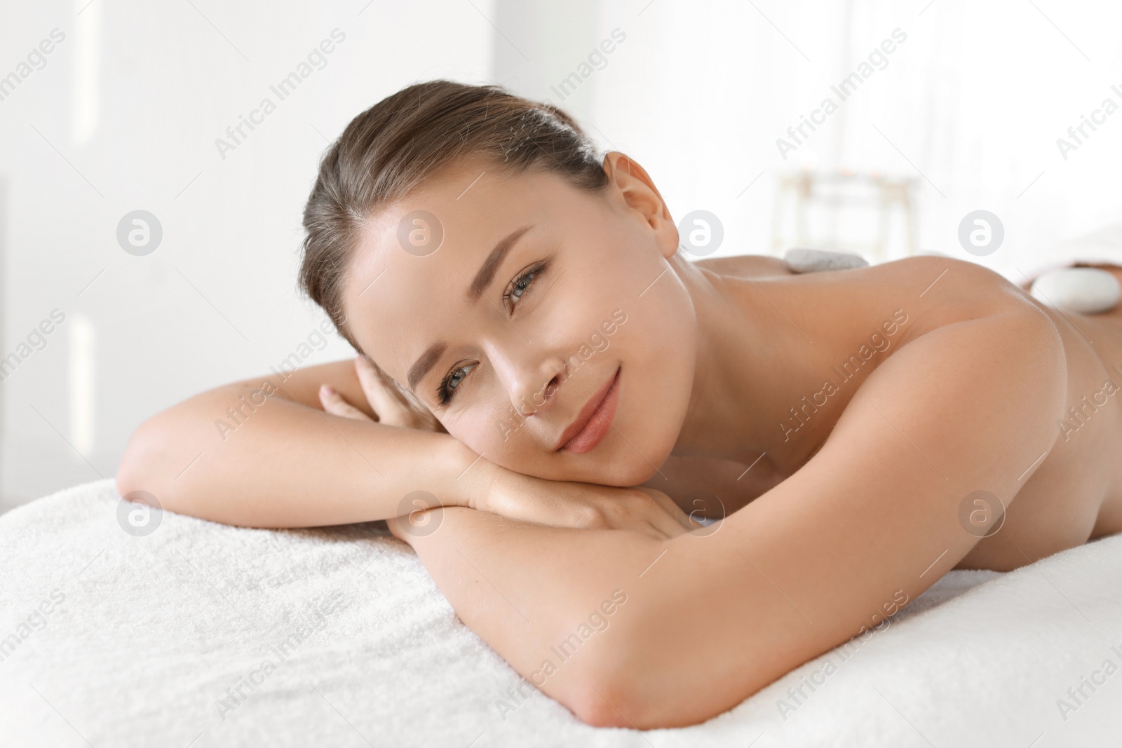 Photo of Young woman with stones on her back in spa salon