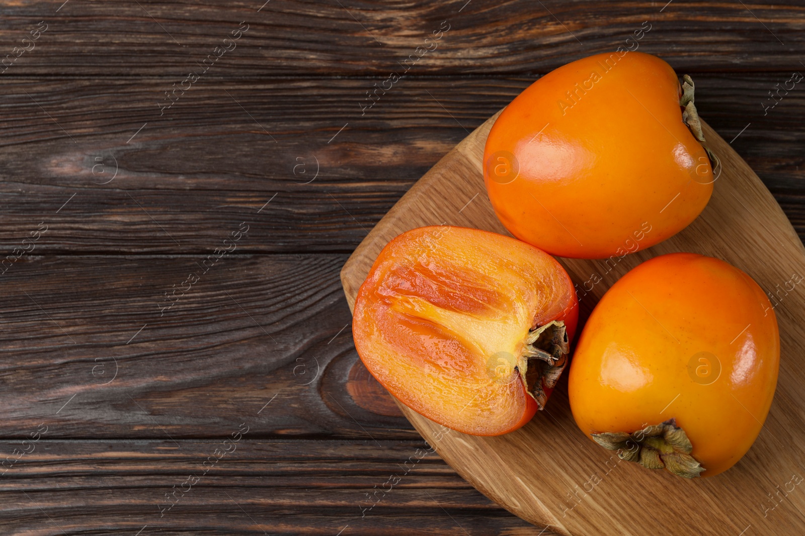 Photo of Whole and cut delicious ripe persimmons on wooden table, top view. Space for text