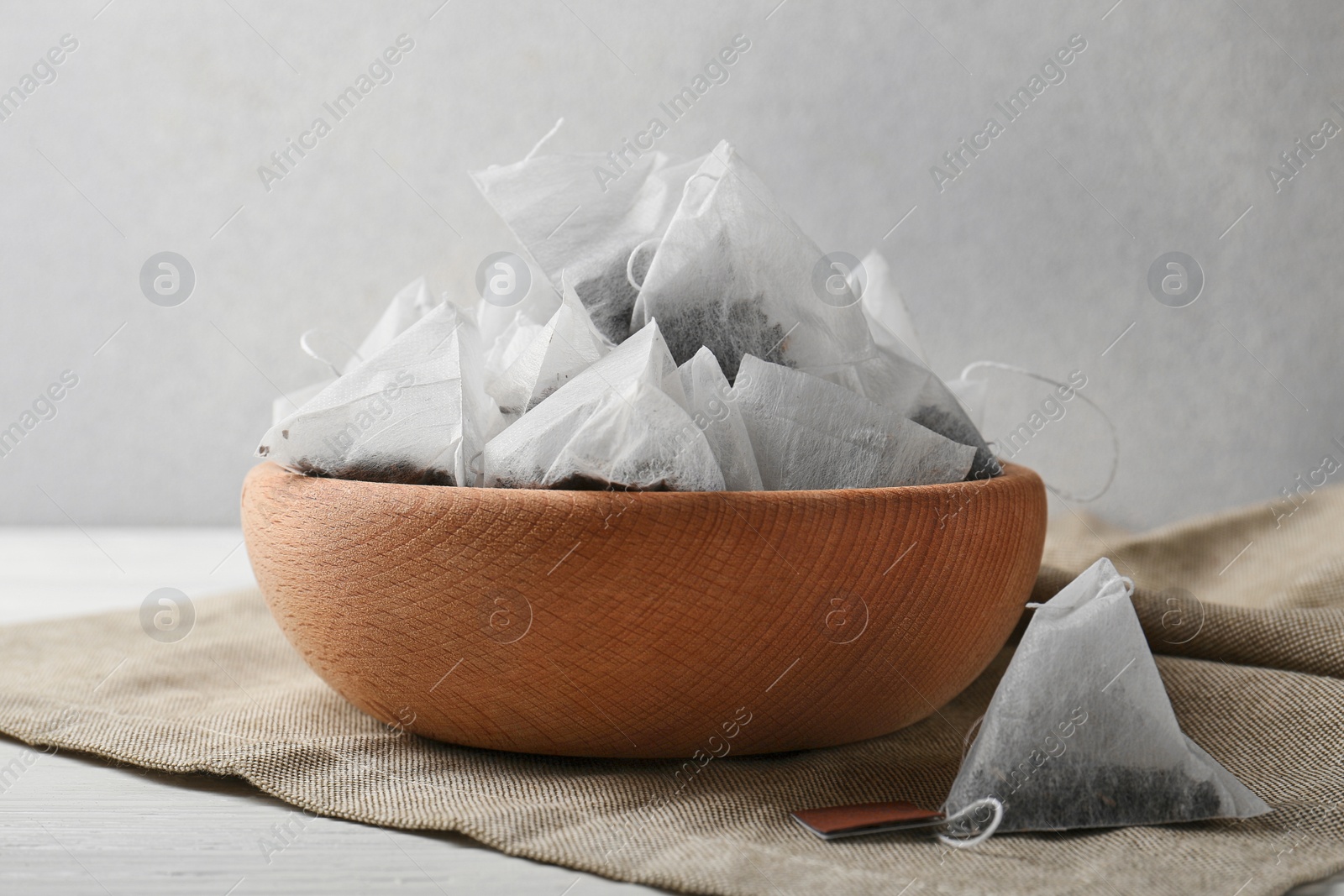 Photo of Bowl with tea bags on white wooden table, closeup