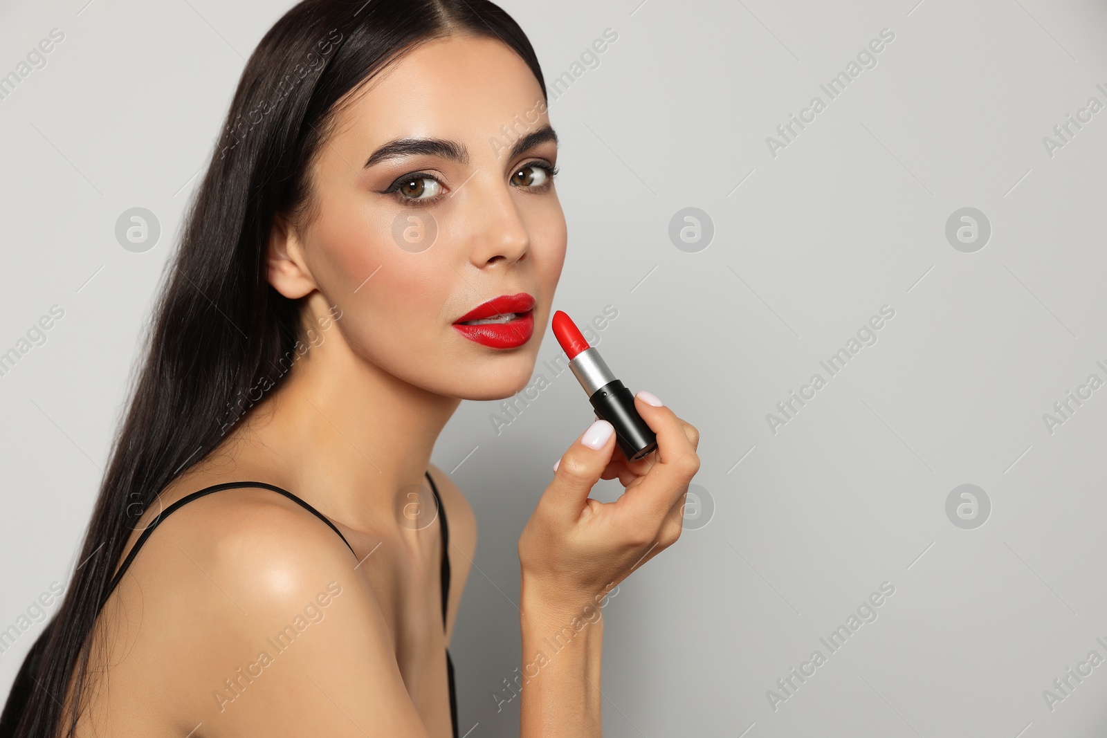 Photo of Young woman with beautiful makeup holding red lipstick on gray background, space for text