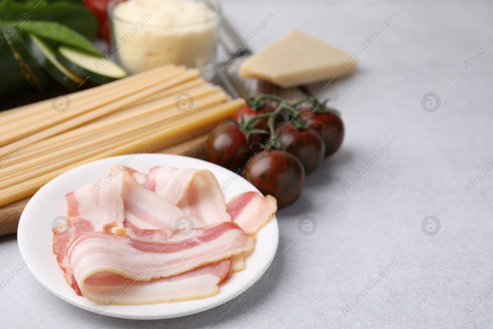 Photo of Raw pasta, bacon and fresh ingredients on light grey table, space for text