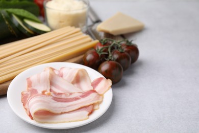 Raw pasta, bacon and fresh ingredients on light grey table, space for text