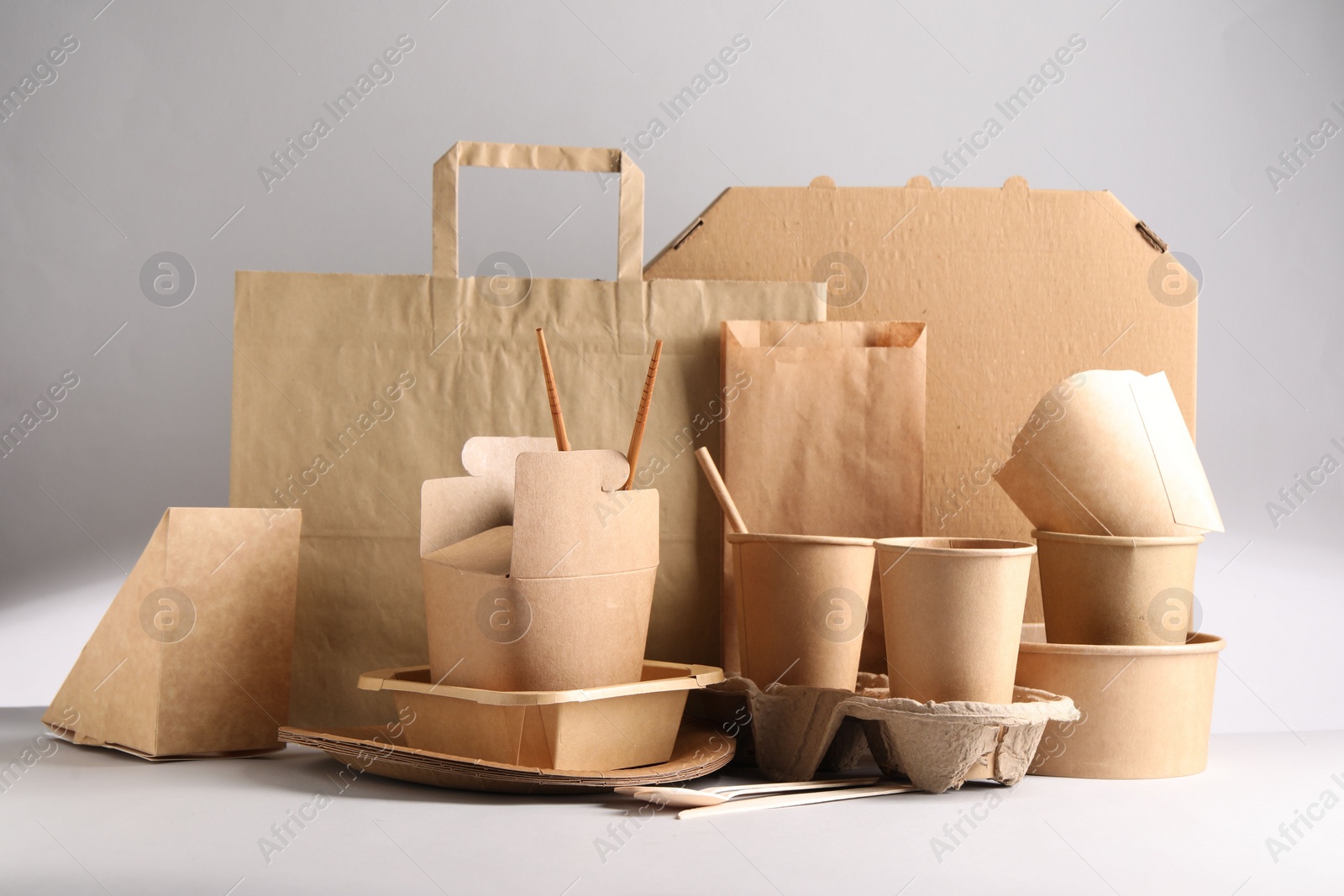 Photo of Eco friendly food packaging. Paper containers, tableware and bag on light background