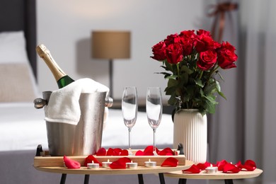 Photo of Honeymoon. Sparkling wine, glasses and bouquet of roses on wooden table in room