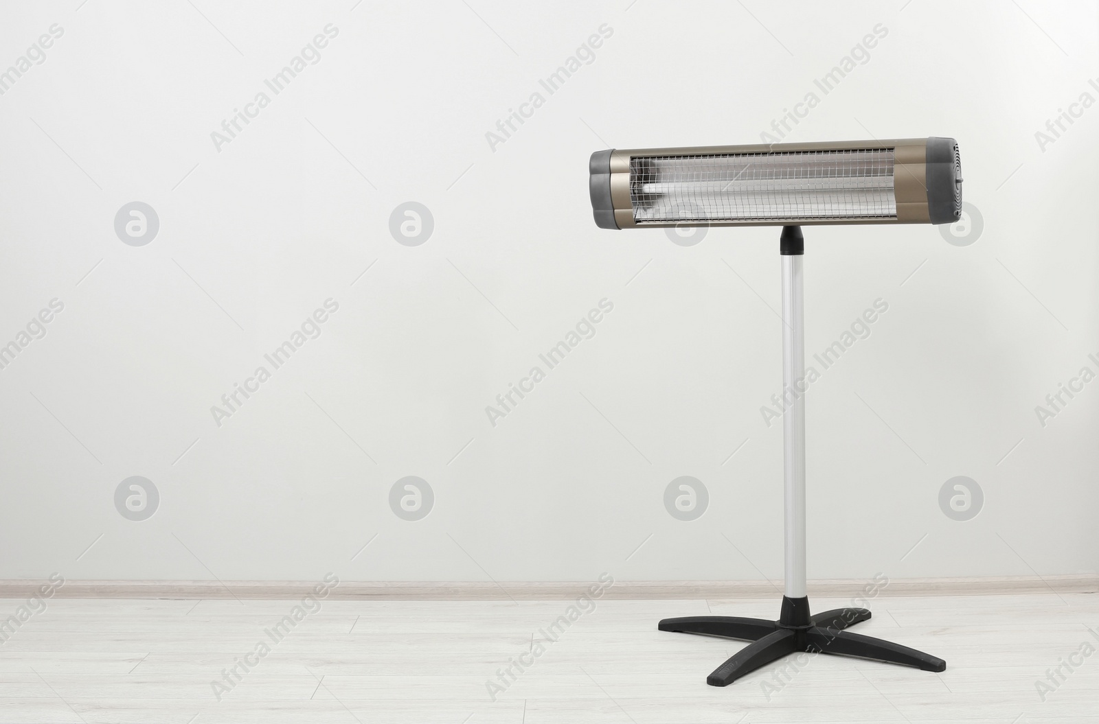 Photo of Electric infrared heater on floor near white wall indoors, space for text