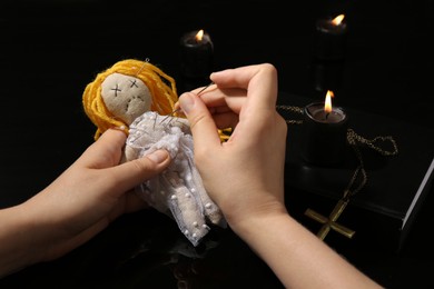 Woman stabbing voodoo doll with pin at black table, closeup. Curse ceremony