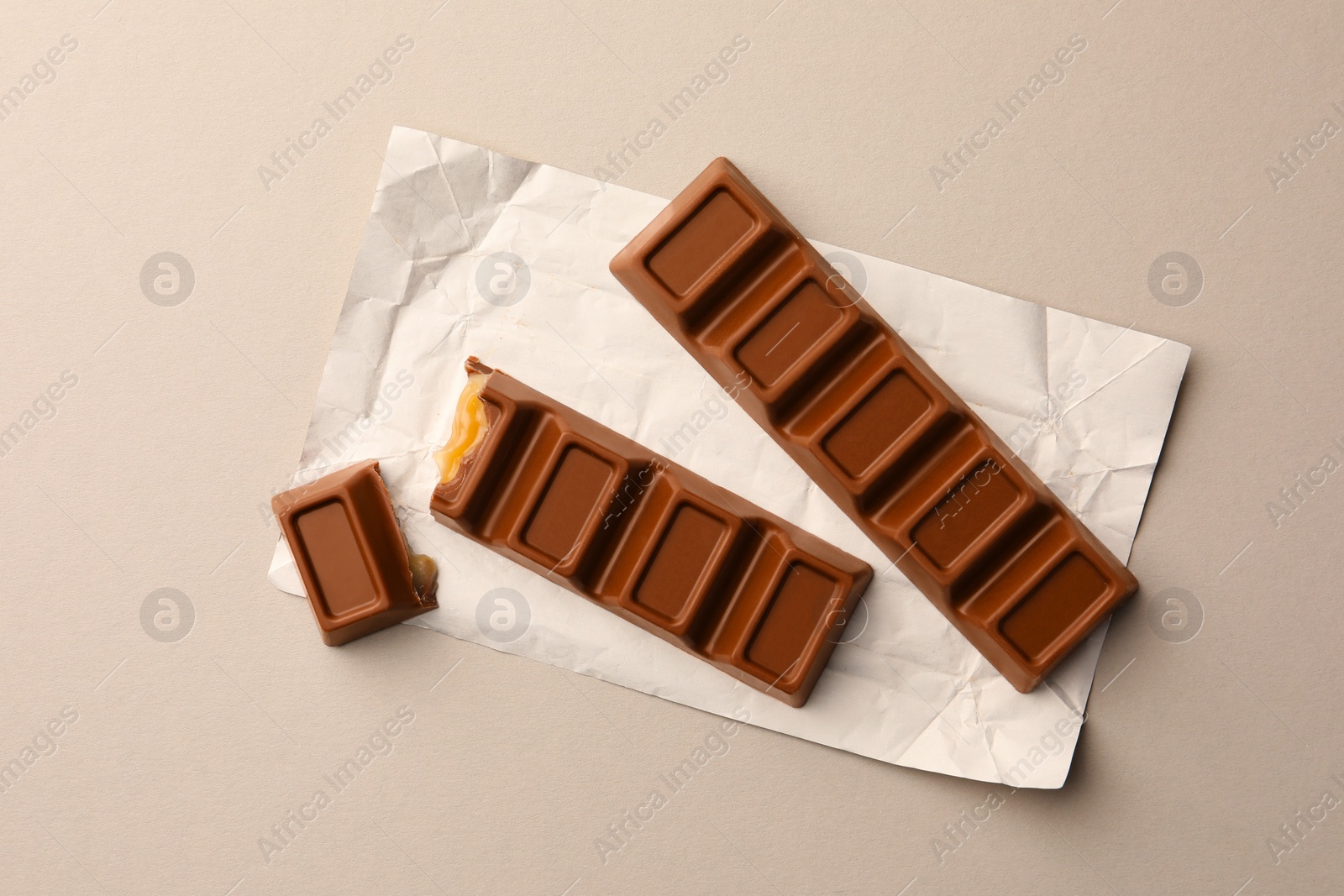 Photo of Tasty chocolate bars with paper wrap on light background, top view