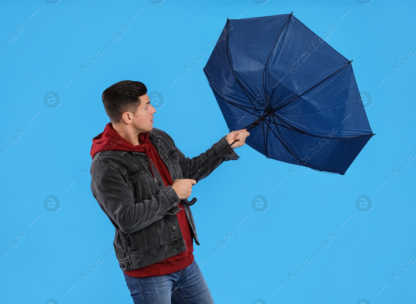 Photo of Man with umbrella caught in gust of wind on light blue background