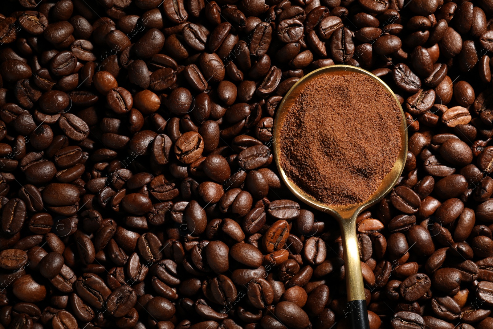 Photo of Spoon with ground coffee on roasted beans, top view. Space for text