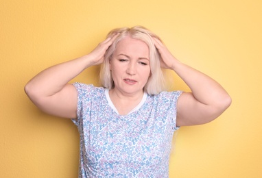 Mature woman suffering from headache on color background