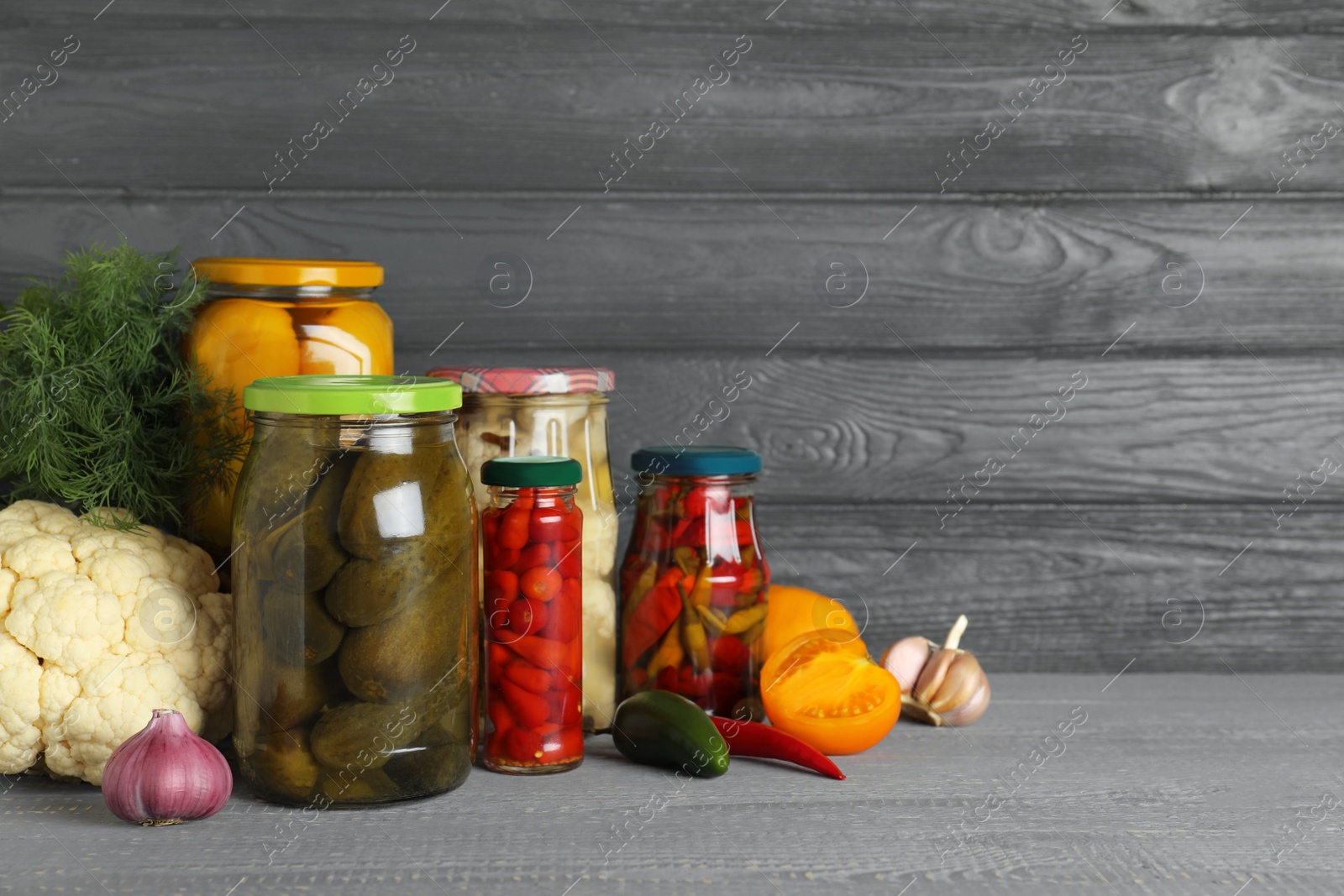 Photo of Glass jars with pickled vegetables on wooden table against grey background. Space for text