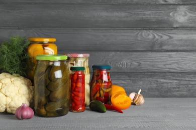 Photo of Glass jars with pickled vegetables on wooden table against grey background. Space for text