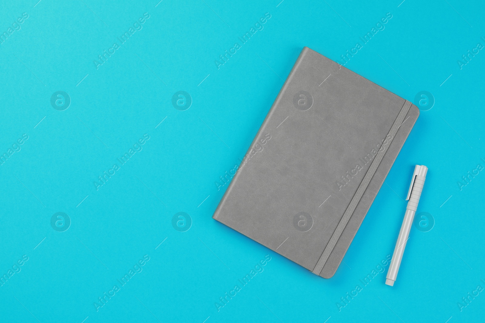 Photo of Gray notebook and pen on turquoise background, flat lay. Space for text