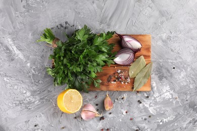 Bunch of raw parsley, lemon, onion, garlic and spices on grey textured table, flat lay