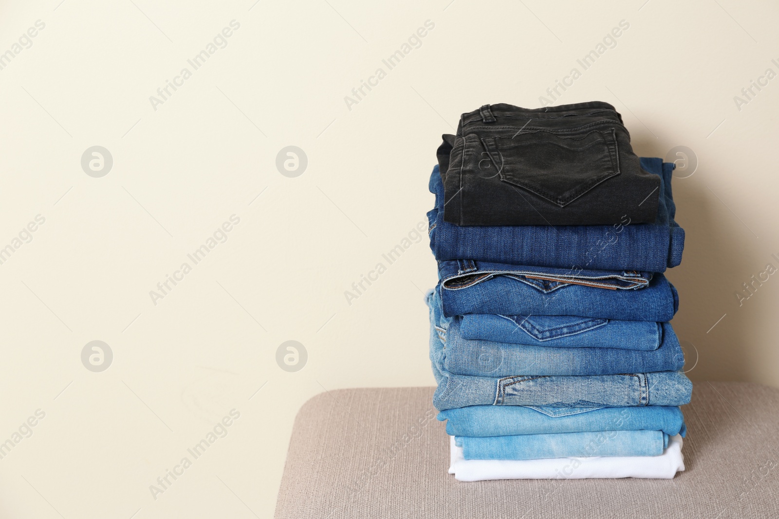 Photo of Stack of different jeans on ottoman against light background. Space for text