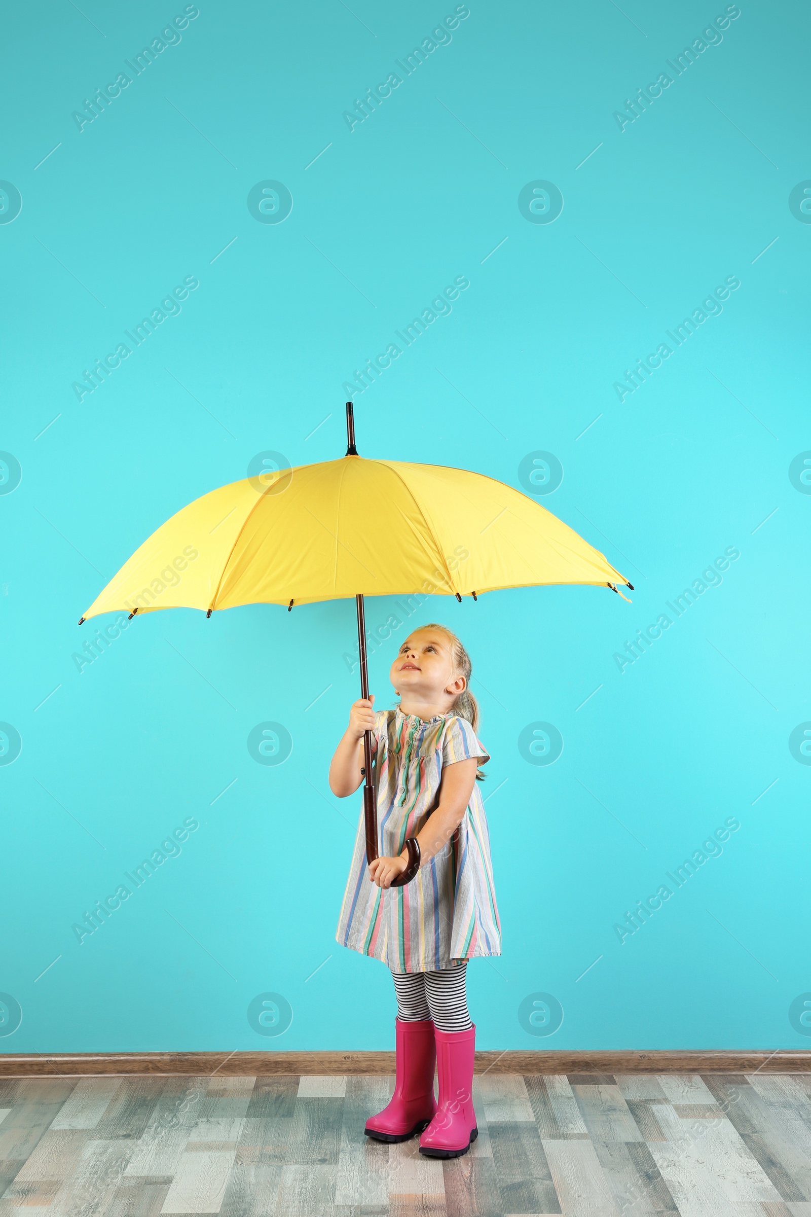 Photo of Little girl with yellow umbrella near color wall