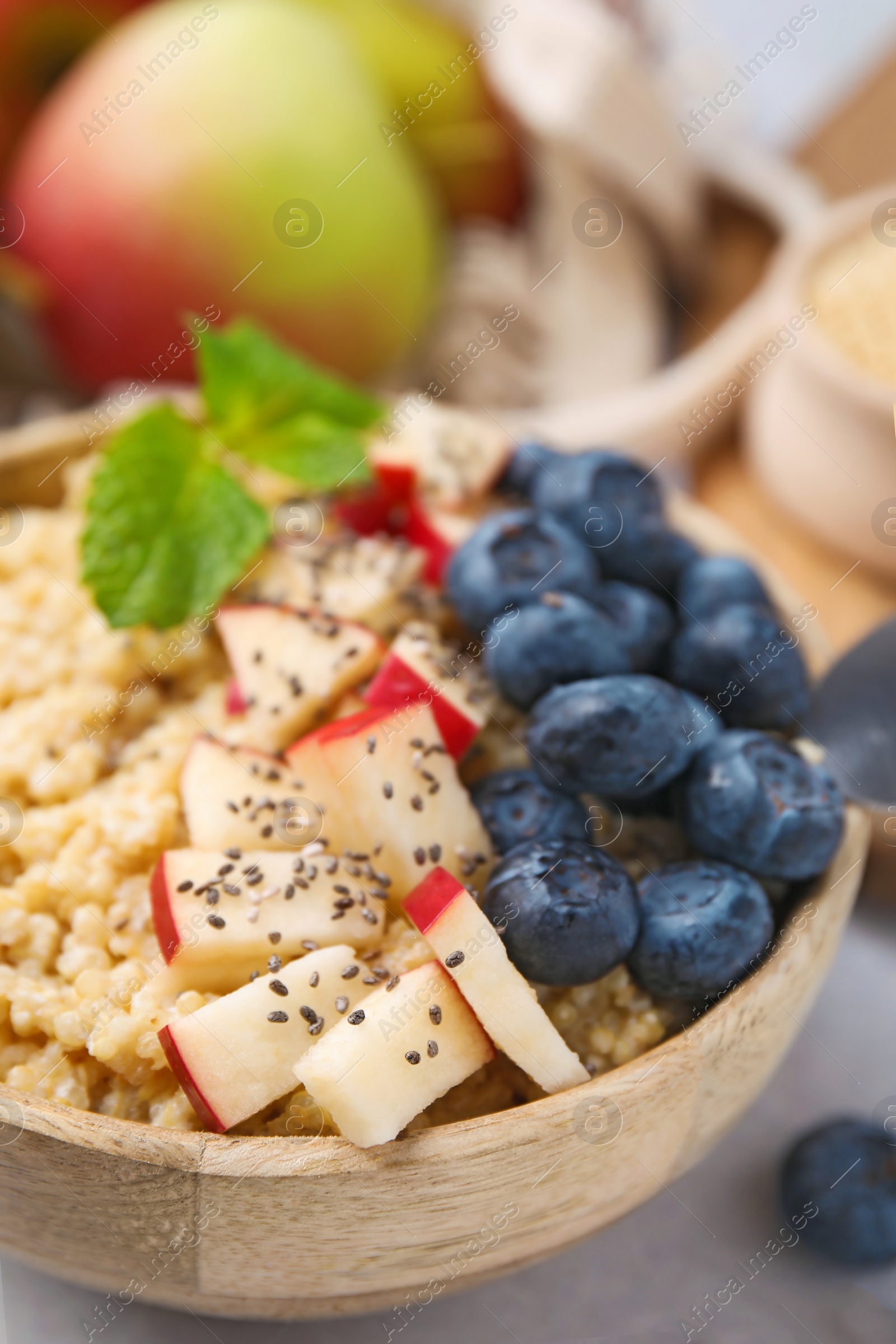 Photo of Bowl of delicious cooked quinoa with apples, blueberries and chia seeds on light grey table, closeup