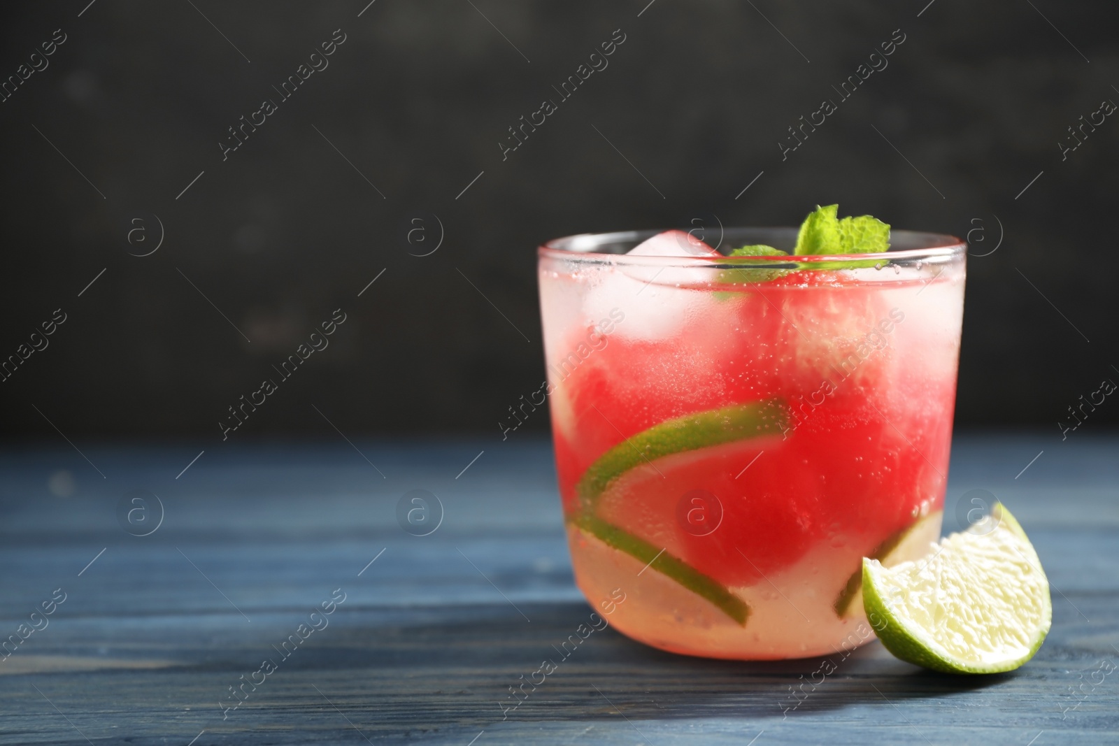 Photo of Glass of refreshing watermelon drink on blue wooden table against dark background. Space for text